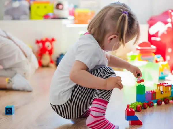 Niña de 0-3 años jugando con bloques de construcción. Crea un tren de juguete y una figura humana.