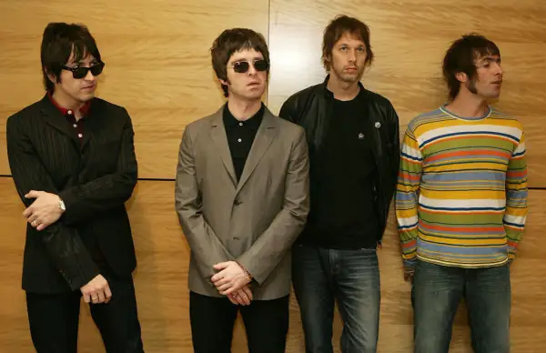 I quattro membri degli Oasis, con i loro look iconici, sembrano pronti per un concerto, un'istantanea degli anni '90.