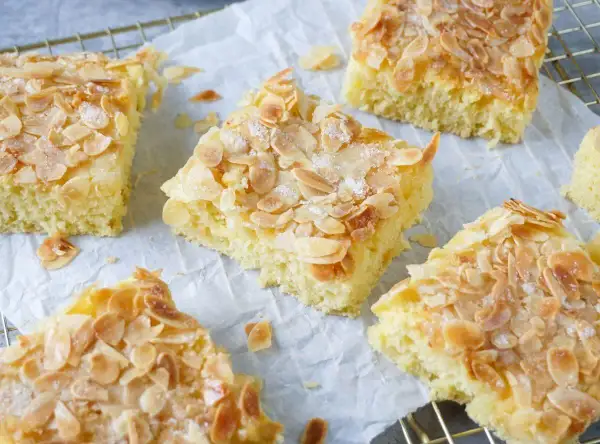Saftiger Buttermilch Kuchen mit knusprigen Mandelblättchen und Zucker bestreut, auf Backpapier und einem Gitterrost.