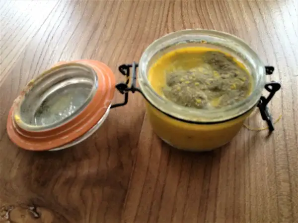 Terrine le parfait recette : un pot en verre avec un couvercle orange ouvert, contenant une préparation jaune et verte sur une table en bois.