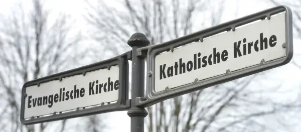 Straßenschilder zeigen "Evangelische Kirche" und "Katholische Kirche". Ein deutlicher Unterschied katholisch evangelisch, der die Vielfalt der Glaubensrichtungen symbolisiert.