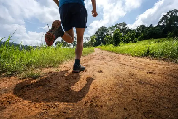 Un coureur sur un sentier de terre, profitant d'un entraînement de renforcement musculaire trail dans un paysage verdoyant.