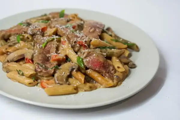 Penne z kawałkami soczystej wołowiny w kremowym sosie z pieczarkami i pomidorkami. Idealne, co w piątek na obiad zamiast ryby.