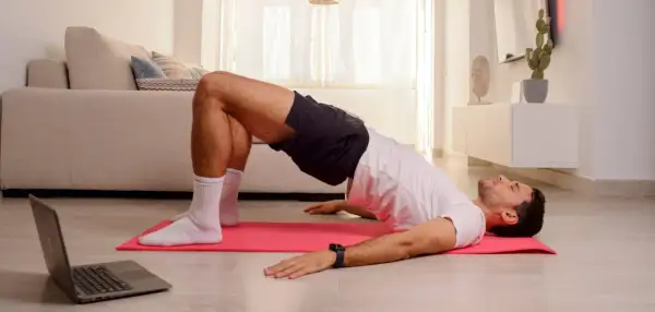 Uomo esegue esercizi di Kegel a casa, seguendo un tutorial su laptop.