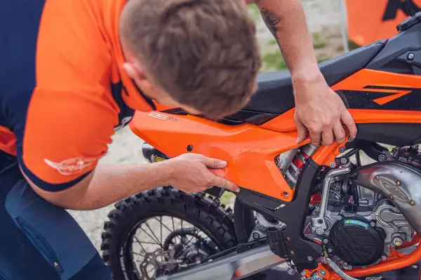 Mecánico ajusta panel en KTM 300 TPI. Se aprecia el motor y la rueda trasera.