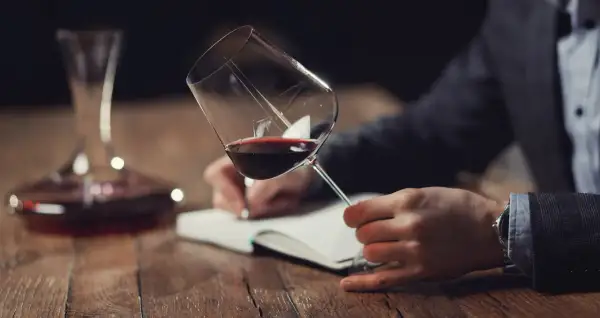 Un homme déguste un verre de vin rouge, notant ses impressions pour la saint-emilion grand cru classé liste.