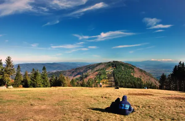 Widok na góry w Bielsku-Białej. Dwie osoby siedzą na trawie, podziwiając jesienny krajobraz i panoramę Beskidów.