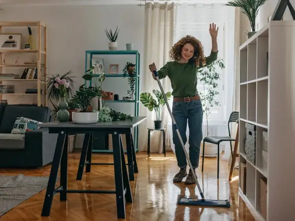 Donna sorridente lava il pavimento con uno straccio, un esempio di come tenere in ordine la casa con gioia.