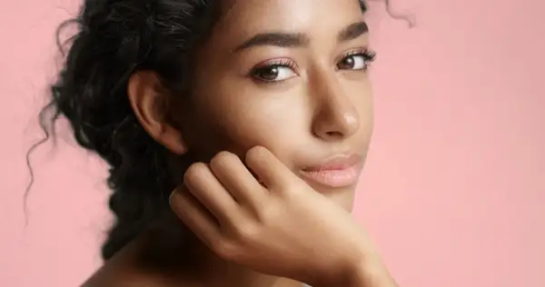 Portrait d'une jeune femme à la peau de couleur de peau olive, aux cheveux sombres et bouclés, posant sa main sur sa joue.