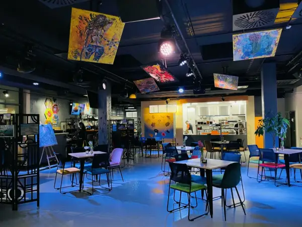 Wnętrze Oria Magic House z kolorowymi obrazami na suficie i ścianach. Stoliki i krzesła tworzą przytulną atmosferę, idealną do przeglądania menu.