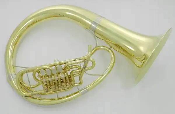 Błyszczący, złoty, duży instrument dęty z zaworami, owinięty wokół ciała muzyka, gotowy do wydobycia głębokich dźwięków.