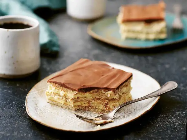 En bit chokladkaka med mariekex och krämig fyllning, perfekt för ett mariekex recept. En kopp kaffe står bredvid.