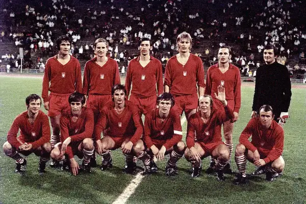 Znani piłkarze reprezentacji Polski w czerwonych strojach pozują na boisku.
