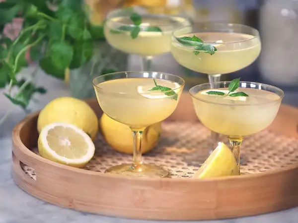 Fyra glas med gyllene limoncello, garnerade med citron och mynta. Perfekt för att lära sig hur dricker man limoncello en varm sommardag.