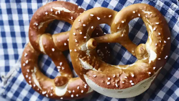 Zwei goldbraune Brezen mit grobem Salz liegen auf kariertem Stoff.