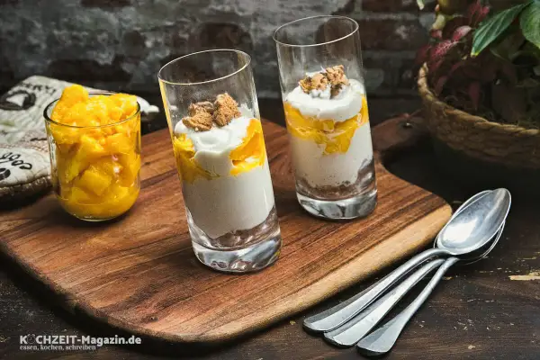 Zwei Gläser mit Mango-Creme und Kekskrümeln, daneben ein Glas mit Mangostücken. Perfekt für leichte ricotta rezepte.