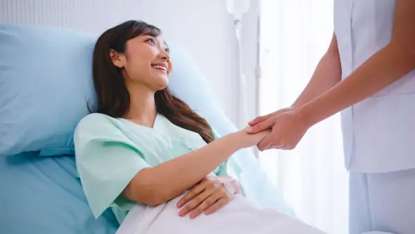 Una paciente sonríe mientras una enfermera le toma la mano, ofreciendo apoyo tras las contracciones después del parto.