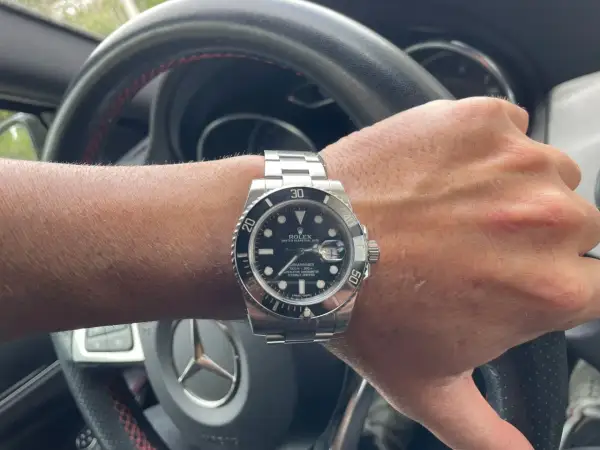 Mano con reloj Rolex Submariner, símbolo de invertir en relojes de lujo. El volante de un coche de alta gama sugiere un estilo de vida exitoso.