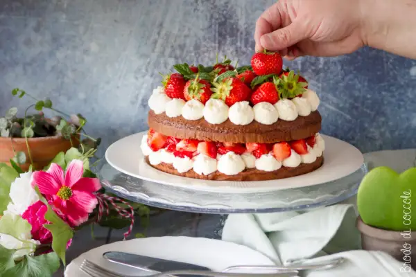Una deliziosa torta con fragole e cioccolato, decorata con panna montata e fragole fresche. Una mano aggiunge l'ultima fragola in cima.
