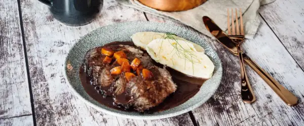 Klassisches Sauerbraten Rezept im Backofen: Zartes Rindfleisch in dunkler Soße mit Karotten und Klößen, garniert mit Dill.