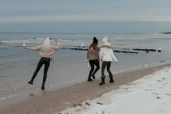Trzy dziewczyny cieszą się zimą nad morzem, biegając po plaży z resztkami śniegu.