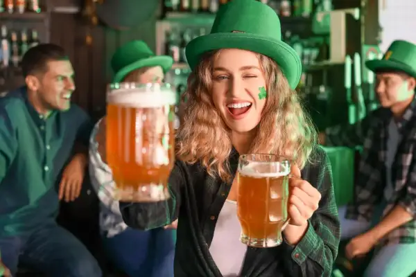 Ragazza con cappello verde e trucco trifoglio offre due boccali di birra irlandese rossa in un pub festoso.
