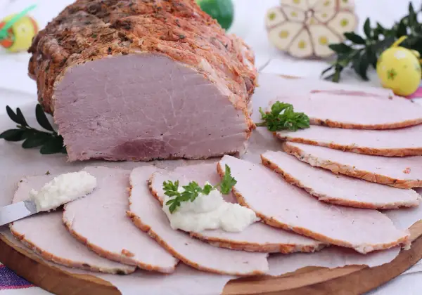 Soczysta szynka pieczona w rękawie, pokrojona w plastry, z chrzanem i natką pietruszki. Idealna na wielkanocny stół.