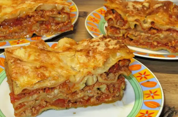 Prosty przepis na lasagne z mięsem mielonym. Pyszne, warstwowe danie z makaronem, sosem mięsnym i serem, podane na kolorowych talerzach.