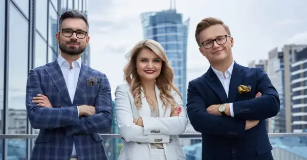 Trzy osoby w eleganckich garniturach stoją na tle nowoczesnych budynków.