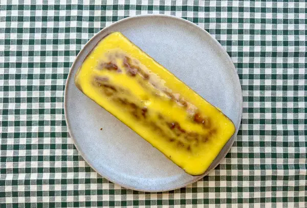 Un delicioso bizcocho de mango y yogur, cubierto con un glaseado amarillo brillante, descansa sobre un plato gris.