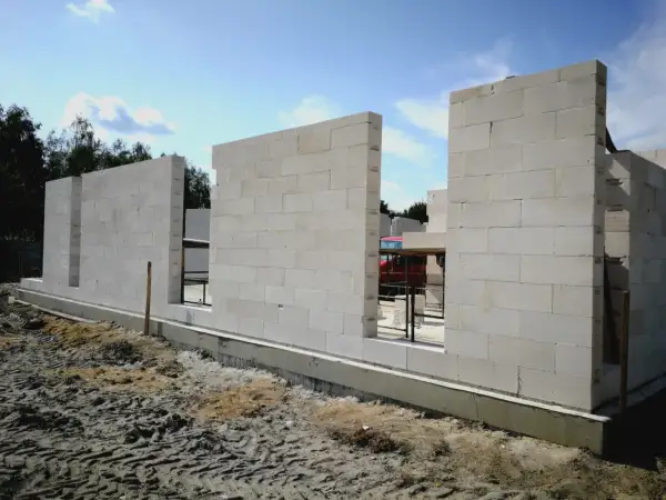 Budowa domu z bloczków z betonu komórkowego. Ściany wznoszą się nad fundamentem, tworząc zarys pomieszczeń.