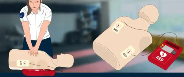 Ilustracja przedstawia manekina do resuscytacji z przyklejonymi elektrodami AED oraz czerwony defibrylator AED.