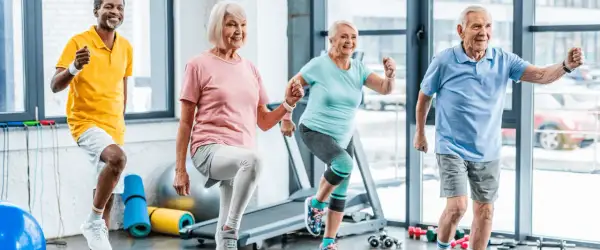 Quatre seniors souriants font de l'exercice ensemble. Voici 5 arguments pour le sport : vitalité, joie, santé, longévité et bien-être.