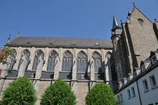 Der Altenberger Dom ragt mit seinen gotischen Fenstern und steinernen Mauern in den blauen Himmel. Grüne Bäume säumen das imposante Bauwerk.