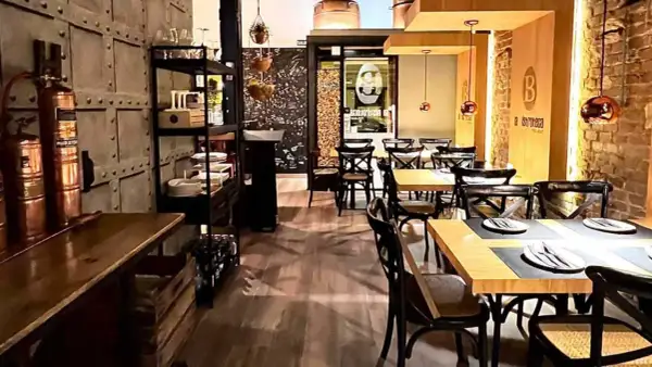 Interior de un bistro bar con mesas puestas, sillas de madera oscura y decoración industrial.