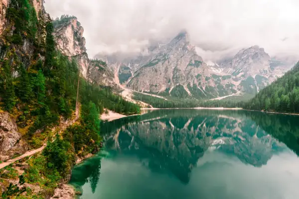 Spokojne Lago di Braies odbija majestatyczne góry i zielone lasy. Ścieżka wije się wzdłuż skalistego brzegu.