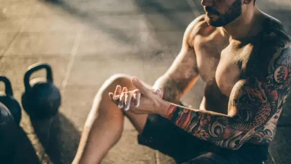 Ein Mann mit beeindruckenden herren tattoos bereitet sich mit Magnesium vor. Kettlebells liegen im Hintergrund.