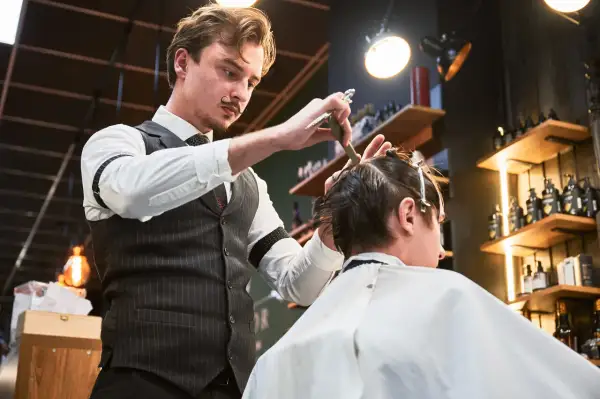 Elegancki barber z wąsikiem precyzyjnie ścina włosy klienta. Kto to? Mistrz fryzjerstwa!
