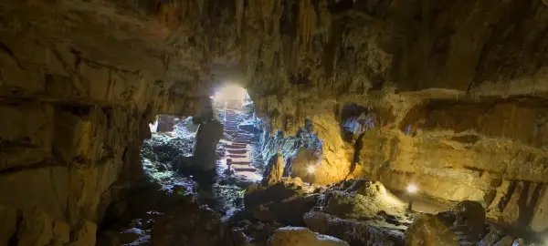 Interior de la cueva del Pindal, con estalactitas, rocas y escaleras iluminadas que conducen a la salida.