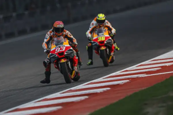 Dos pilotos de MotoGP compiten en una carrera. El piloto número 93 de Repsol Honda lidera, seguido de cerca por el piloto número 36. El coste de una moto de MotoGP es altísimo.