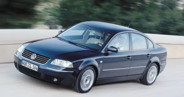 Ciemnoniebieski VW Passat W8 z jasnym wnętrzem mknie po drodze, za kierownicą siedzi mężczyzna.