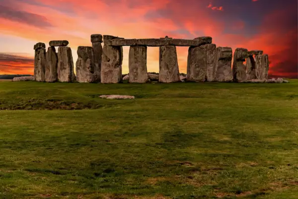 Las imponentes piedras de Stonehenge en Inglaterra se alzan contra un cielo crepuscular de tonos naranjas y rojizos, un misterio ancestral bajo la luz del atardecer.