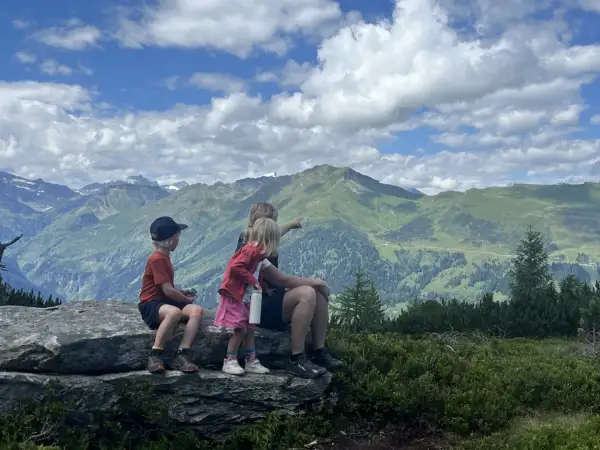 Familj njuter av en fantastisk utsikt under en bad gastein vandring. Barnen pekar ut över de gröna bergen och molnen.