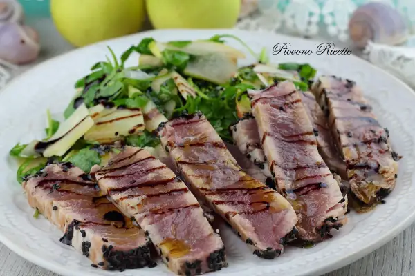 Deliziosa tagliata di tonno scottata, cosparsa di semi di sesamo nero, servita con un'insalata fresca di rucola e scaglie di parmigiano.