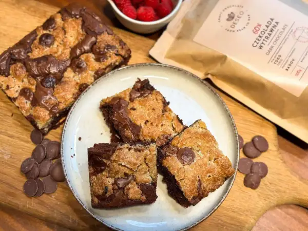 Pyszne brookies z kawałkami czekolady, obok maliny i opakowanie ciemnej czekolady.