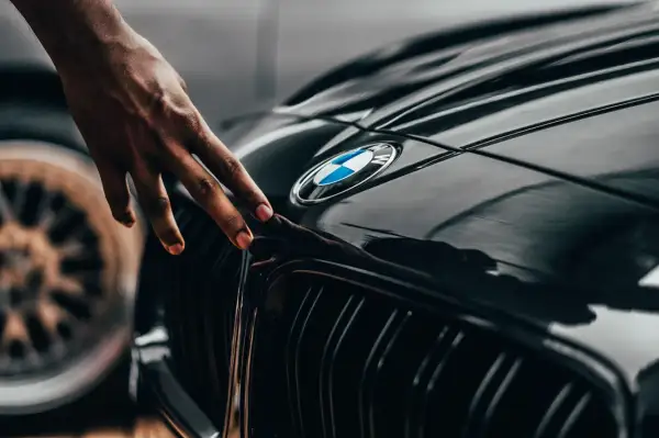 Dłoń dotyka błyszczącej maski czarnego BMW. Zastanawiasz się, ile schnie lakier bezbarwny po polerowaniu?