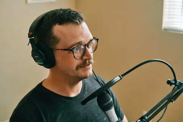 Mężczyzna w słuchawkach i okularach z wąsami ustawia mikrofon.