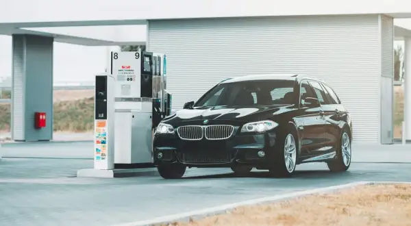 Czarne BMW na stacji paliw. Przykład, jak odliczyć 50% VAT od paliwa, może być związany z kosztami podróży służbowych.