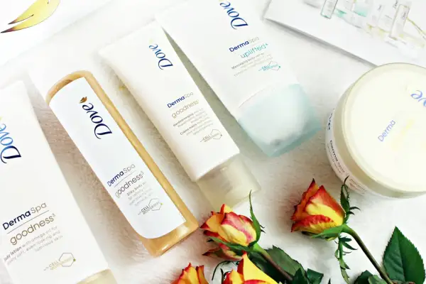 Krem do rąk, olejek i balsam do ciała z serii Dove DermaSpa Goodness, otoczone płatkami róż.