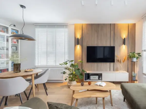 Przytulny salon inspiracje: drewniana ściana z TV, okrągły stół z krzesłami, rośliny i stylowe oświetlenie tworzą ciepłą atmosferę.